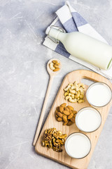 Nut milk in glasses on wooden board on concrete background. Top view, space for text.