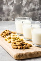 Almonds, cashew, walnuts and nut milk in glasses on wooden board on concrete background. Selective focus, copy space. 