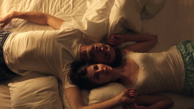 Happy couple lies in the bed on the back and talking before sleeping.