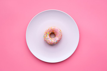 Sweet tasty snack. Glazed donut on plate on pink background top view copy space