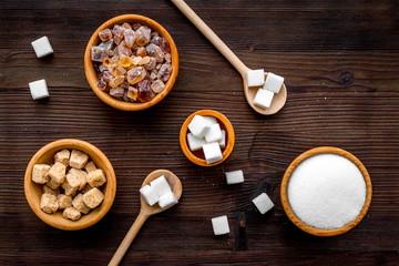 Sugar background on dark wooden table. Bowls with different kinds of sugar. Top view