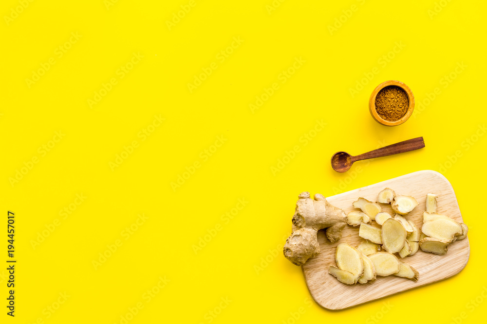 Wall mural Spice and condiment. Ground ginger in small bowl near sliced ginger root on cutting board on yellow background top view copy space