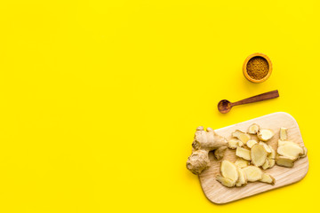 Spice and condiment. Ground ginger in small bowl near sliced ginger root on cutting board on yellow background top view copy space
