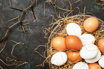 Multicolored chicken eggs with straw and branches, spring Easter composition, black background, top view
