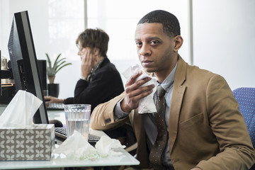 Business man working at his desk sick with a cold and fever