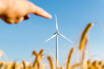 Hand pointing at a wind turbine with golden corn field in the foreground
