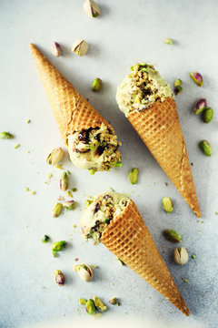 Green ice cream in waffle cone with chocolate and pistachio nuts on grey stone background. Summer food concept, copy space. Healthy gluten free ice-cream. Banner