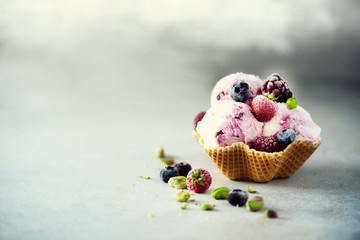 Pink ice cream with berries, strawberries, blueberries, raspberries, pistachios in waffle basket. Summer food concept, copy space. Healthy gluten free fruit ice-cream. Banner