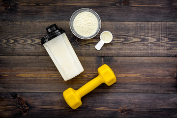 Nutrition for muscle growth. Scoop of protein near shaker, dumbbell on dark wooden background top view