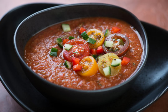 Cold spanish tomato soup gazpacho served in a black bowl, close-up, selective focus, horizontal shot