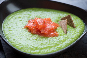 Close-up of green peas cream-soup topped with salmon fillet, selective focus