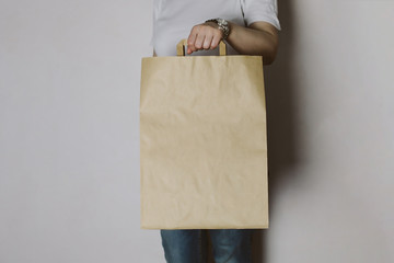 Fototapeta na wymiar Girl is holding blank craft paper bag, design mockup. Handmade shopping bag for gift or food.