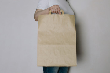 Young hipster girl holding blank big craft shopping bag, mock-up of craft paper package with handles. Shopping, sale concept.