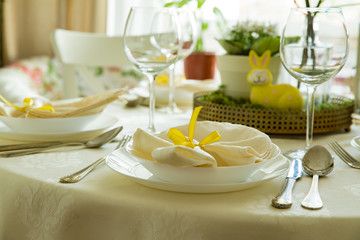 Beautiful served round table with decorations in dining room. Little yellow bunny, willow branches decorated with colorful Easter eggs. Spring holiday setting. Close-up
