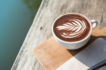 Vintage of hot coffee cup cappuccino art, spoon, tissue, chopping board on wooden table with copy space and the river background. positive thinking concept