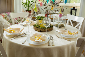 Beautiful served round table with decorations in dining room. Little yellow bunny, willow branches decorated with colorful Easter eggs. Spring holiday setting