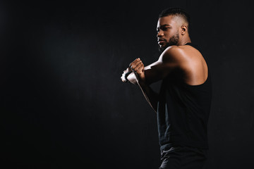 Fototapeta na wymiar side view of athletic young african american man stretching muscles isolated on black