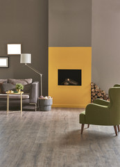 modern living room with fireplace. Brown and yellow stone wall. grey sofa and green armchair decoration with lamp and frame.