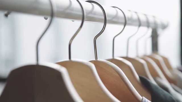 On the floor stand (rave) for clothes hanging wooden hangers with things. Hanger with women's clothes of different colors against the background of a panoramic window, close-up. Woman wardrobe.