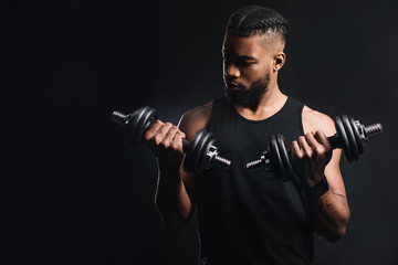 Fototapeta na wymiar handsome muscular african american man exercising with dumbbells isolated on black