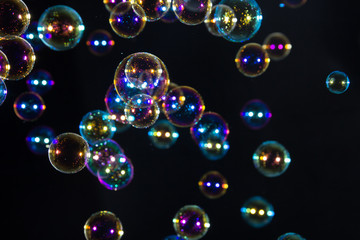 Abstract bright rainbow soap bubbles floating in the dark.