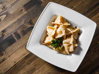 Meat dumplings - russian pelmeni, ravioli with meat on plate on a wooden background