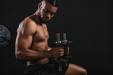 side view of muscular shirtless young african american man exercising with dumbbells on black