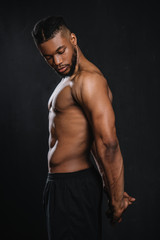Fototapeta na wymiar side view of shirtless muscular young african american man stretching hands isolated on black