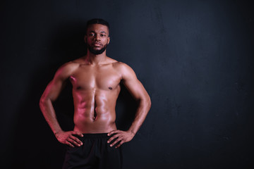 Fototapeta na wymiar muscular bare-chested african american man standing with hands on waist and looking at camera isolated on black