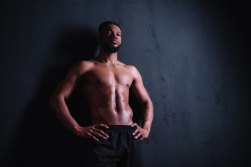 Fototapeta na wymiar low angle view of muscular shirtless young man standing with hands on waist and looking away on black