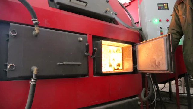 Man opens the door of an industrial boiler. Alternative fuel burns in a boiler