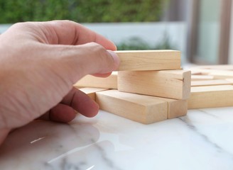 Building wooden block puzzle on the marble table / Copy space and Closeup hand try to build the blocks wood game / concept of building and construction