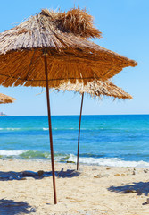 Straw beach umbrellas. Sand, blue sea and clear sky. Selective focus on the parasols