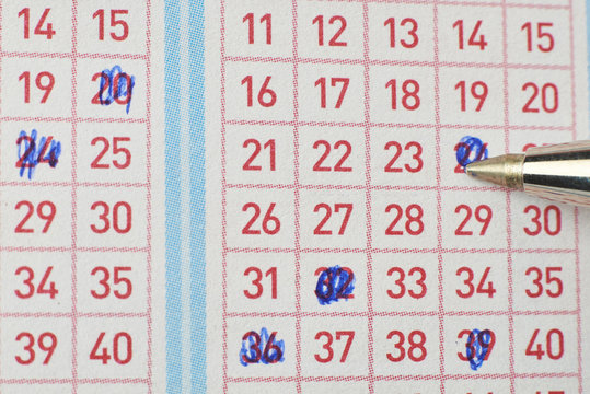 Closeup of hand marking number on lottery ticket with pen.