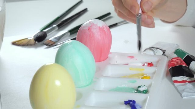 A woman paints Easter eggs with colored paints, close-up