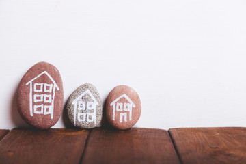 Three houses drawn on stones over brown wood and white background