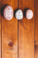 Three houses drawn on stones over brown wood.