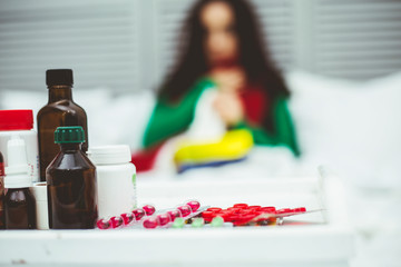 Table with medicines, pills and sprays against the background of a young sick girl in bed. The concept of health and disease.
