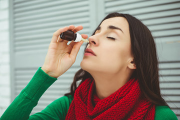 Spray for the nose. Photo of a young sick woman in a red scarf which treats the nose with a spray....