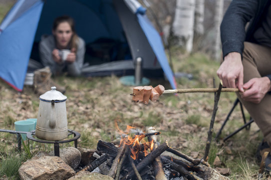 couple preparing dinner on campfire near camping tent during autumn cold season
