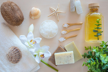 Wellness setting. Sea salt in glass, soap, towel, olive oil and flowers on white textured background. Space for copy. Flat lay