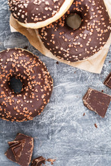 Three chocolate donuts over a grey textured background. Flat lay. Copy space.