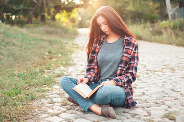 A young female is sitting on ground and reading book