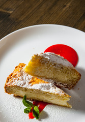 Piece of cake on plate with strawberry sauce on a wooden background