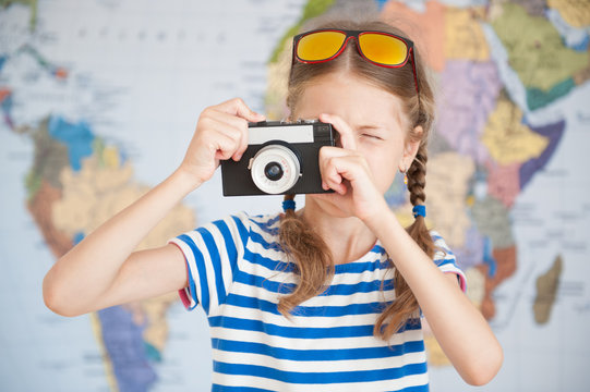 pretty little girl in striped T-shirt takes picture on vintage camera on the background of world map