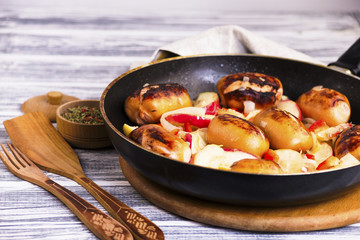 Fried pork sausages with apples and onions in a frying pan