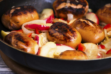 Fried pork sausages with apples and onions in a frying pan