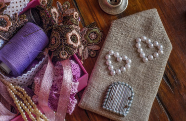 A collection sewing accessories and objects in lilac and pink colours on a old wooden background. Top view. Flat lay.