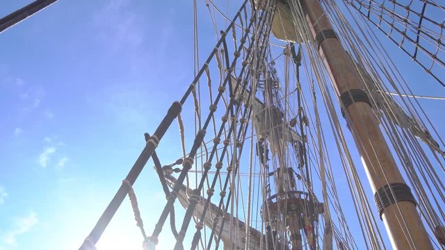 sailors climb up the mast on a rope ladder on a traditional sailing ship.