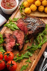 Wall murals Steakhouse Juicy tasty grilled fillet steak served with tomatoes and cheese balls  on an old wooden board.
